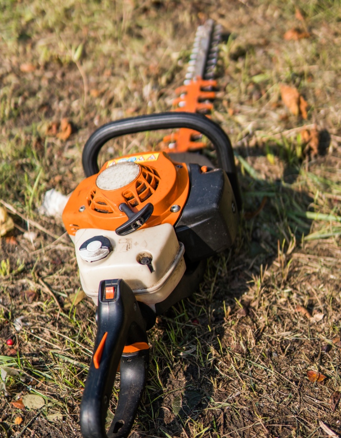 Taille-haie thermique orange posé sur un sol extérieur